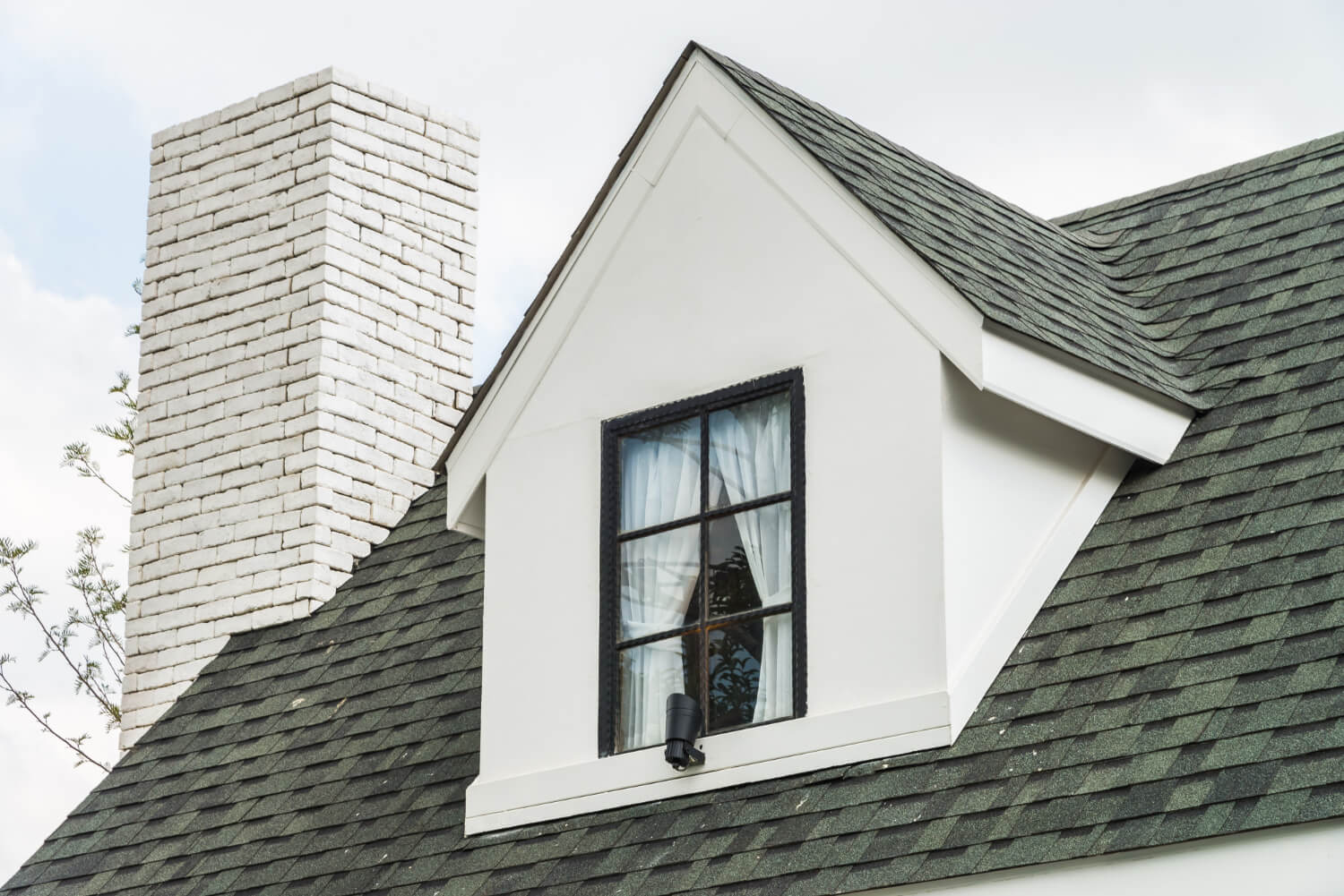 Close-up exterior of a residential roofline, dormer window, and white brick chimney matching main house architectural styles for an ADU build.